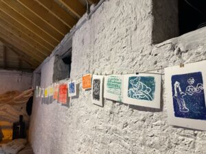 Prints and artwork hanging on a string against a white stone wall